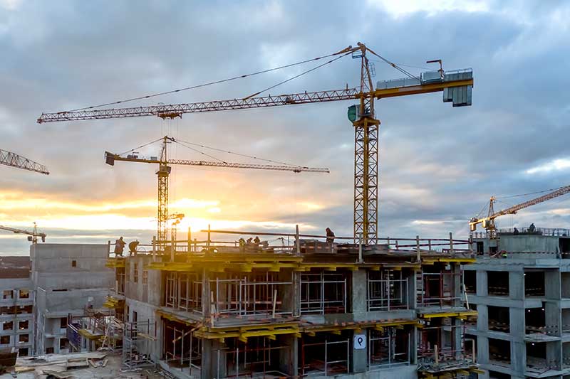 construction loan lenders - photo of new building under construction with giant cranes, at sunset.