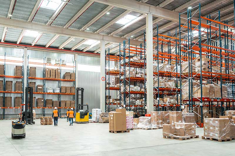 industrial and manufacturing investment loans - In this photo, Warehouse workers are managing logistics, operating forklifts, and organizing packages on shelves in a distribution center.