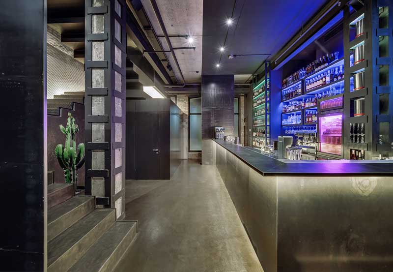 restaurant loans and financing - photo description: Luminous restaurant in a loft style with brick and concrete walls, column, stairway and a glossy floor. There is a bar rack, shelves with bottles and glasses, fridge, bar equipment, big cactus.